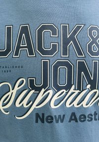 Blue cotton t-shirt featuring bold black and white text, including "JACK & JONES" and "Superiors," with a smooth texture and casual design.