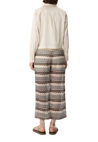 Kremowa koszula z kołnierzykiem i szerokie spodnie w wzór zygzak w odcieniach brązu, beżu i bieli; całość dopełniają brązowe sandały.