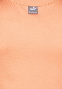 Pomarańczowy, teksturowany materiał Puma z okrągłym dekoltem i metką z logo marki. Materiał wydaje się oddychający i lekki.