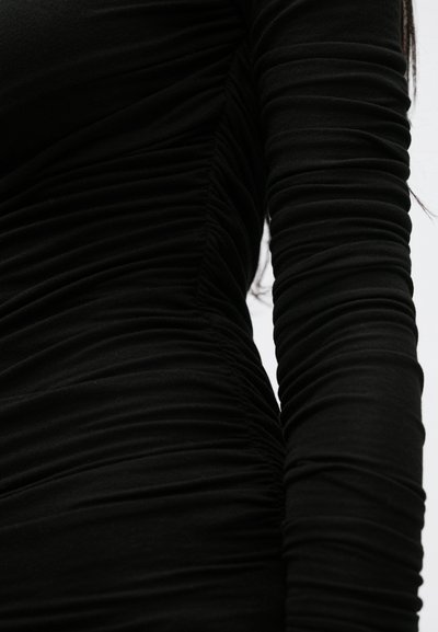 Vestido preto de manga comprida com um design texturizado franzido, apresentando tecido reunido ao longo dos lados e das mangas para uma silhueta justa ao corpo.