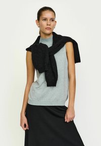 Top gri fără mâneci din material moale, cu guler înalt, purtat cu un pulover negru legat la umeri și o fustă neagră.