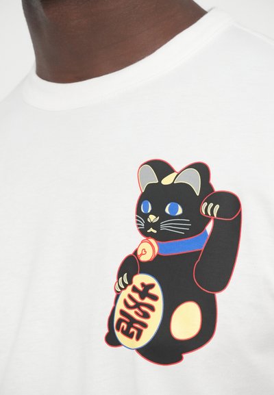 Λευκό T-shirt με ένα μαύρο γατί με μπλε μάτια, μπλε κολάρο και υψωμένο πόδι, που κρατάει ένα στρογγυλό σήμα με κείμενο.