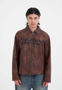 Brun læderjakke med lynlås, krave og broderet "Ed Hardy 1971" i sort. Har en struktureret overflade og en afslappet pasform.