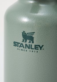 Green textured metal water bottle featuring a logo of a bear with wings and the brand name "STANLEY" with the text "SINCE 1913" beneath.