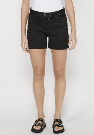 Black denim shorts with a belt, front pockets, and rolled hem. Worn with black sandals featuring decorative hardware accents.