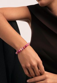 Pulsera de cuentas que presenta tonos variados de piedras rosas y moradas, con superficies suaves y un diseño flexible. Acentos dorados entre las cuentas.