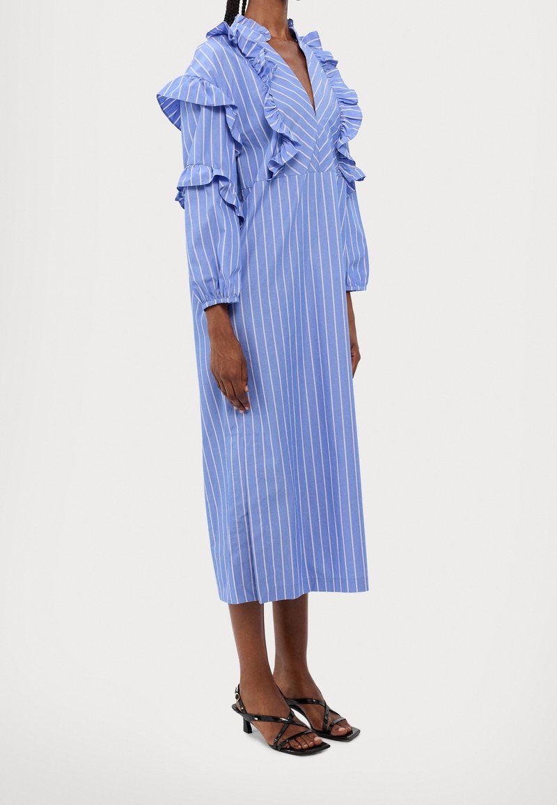 Blå randig klänning med volanger vid halsringningen och ärmarna, midilängd, tillverkad av lättviktigt tyg; matchas med svarta remsandaler.