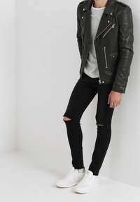 Veste de moto en cuir noir avec quincaillerie en argent, t-shirt rayé gris, skinny jeans noirs déchirés, et baskets blanches.
