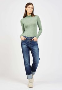 Green long-sleeve turtleneck top paired with high-waisted blue jeans, cuffed at the ankles, and cream-colored lace-up boots.