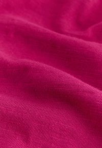 Tissu rose vif avec texture tricotée visible et plis doux créant des ombres douces et des reflets.