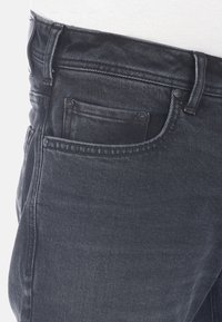 Jeans de mezclilla negra con corte ajustado, que cuentan con una cinturilla clásica, diseño de cinco bolsillos y detalles de costura sutiles.