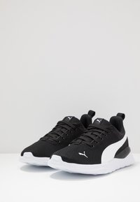 Black mesh sneakers with white accents, rounded shape, flexible sole, and reinforced heel, featuring lace-up closure and logo detail.