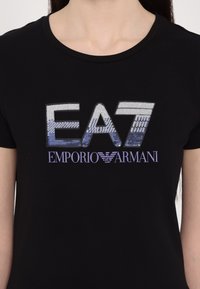 Zwarte katoenen t-shirt met een glanzend, metallic logo "EA7" in een gradient van zilver naar blauw en de merknaam "EMPORIO ARMANI" eronder in paars.