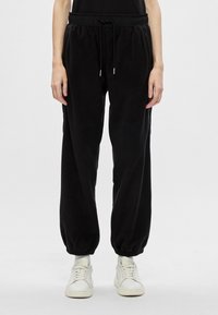 Czarne dresowe spodnie z miękkiego materiału, z elastycznym pasem, regulowanym sznurkiem w talii i zwężanymi mankietami, połączone z białymi sneakersami.