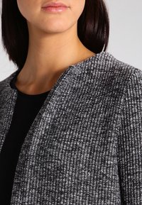 Szary kardigan teksturowany z otwartym dekoltem, z dzianinowym wzorem ryżowym. Materiał ma miękki, dziany wygląd.