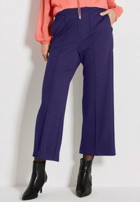 Marinefarbene weit geschnittene Hose mit hoher Taille, ausgestattet mit Stichdetails und einer glatten Textur, kombiniert mit schwarzen Knöchelstiefeln.