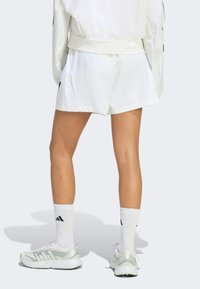 Bijele sportske kratke hlače labavog kroja sa suptilnim sjajem, uparene s bijelim i srebrnim tenisicama te bijelim čarapama srednje duljine s crnim logom.