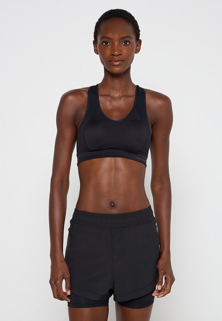Czarny stanik sportowy z plecami w stylu racerback, wykonany z gładkiego materiału. W połączeniu z czarnymi szortami z miękkim paskiem w talii i warstwowym wykończeniem.