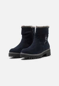 Bottines bleu marine en daim avec un col en fourrure, une fermeture éclair latérale et une semelle en caoutchouc noir texturée dotée de crampons profonds pour une meilleure adhérence.