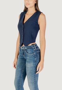 Gilet ajusté bleu marine avec un design cintré, cinq boutons et une poche avant, porté sur un jean bleu clair à coupe classique.