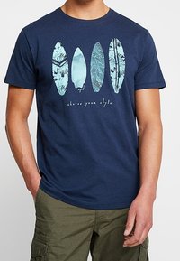 Camiseta de algodón azul marino con un gráfico frontal de cuatro tablas de surf en tonos aqua con diferentes patrones y el texto "elige tu estilo".