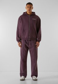 Lilla zip-up hoodie med forlommer og snøredragt, begge i et blødt materiale. Har let syning og kontrasterende grå detaljer.