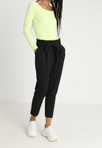 Paita hiraa pituisilla hihoilla, lime vihreä, yhdistetty korkeavyötäröisiin mustiin housuihin, joissa on solmittava vyö, ja täydentää ilmettä valkoiset tennarit.