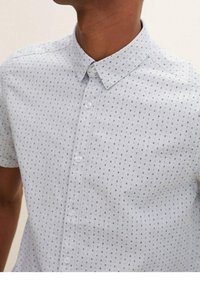 Camicia a maniche corte di colore azzurro chiaro con colletto a bottoni, caratterizzata da un motivo a piccole quadrati in blu scuro e grigio.