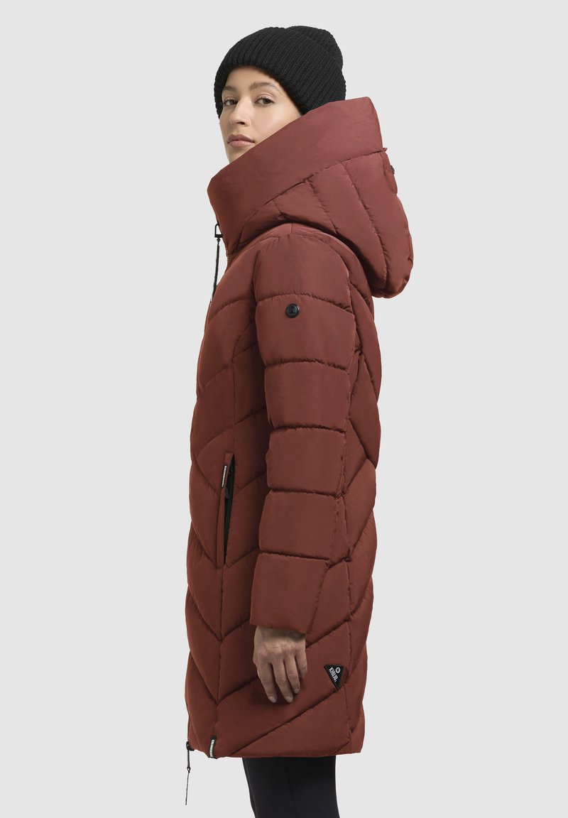 Parka bordeaux trapuntato con colletto alto e cappuccio. Presenta dettagli in nero, tasche laterali e una toppa con logo vicino all'orlo. Texture liscia.