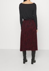 Sort langærmet top parret med en flydende rød og sort ternet nederdel. Nederdelen har et plisseret design, der falder til midt på læggen.