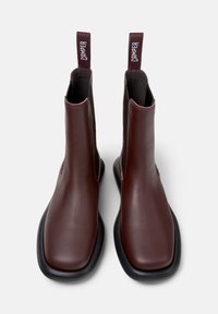 Braune Leder Stiefeletten mit elastischen Seiteneinsätzen, schwarzen Gummisohlen und Stoffzuglaschen, die an der Ferse mit "CAMPER" gekennzeichnet sind.