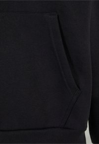 Sweat-shirt noir avec poche kangourou, ourlet et poignets côtelés, fabriqué en tissu doux et texturé. Le design est minimaliste et fonctionnel.