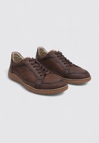 Zapatillas de cuero marrón con una textura suave, punta redonda, sistema de cordones y suelas de goma en contraste. Presentan perforaciones en la parte superior.