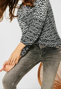 Svart och vit mönstrad långärmad topp med ballongärmar, i kombination med grå denim skinny jeans med en strukturerad textur.