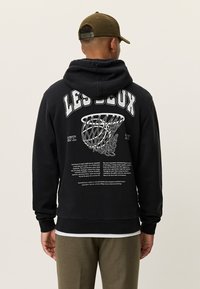 Μαύρο φούτερ με κουκούλα και κορδόνι. Φέρει το κείμενο "LES DEUX" και μια γραφική απεικόνιση μπάσκετ στην πλάτη, με επιπλέον περιγραφικό κείμενο από κάτω.