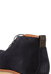 Botas de tobillo de ante azul marino con punta redonda, forro de cuero marrón claro en contraste y un tirador texturizado con marca en relieve.