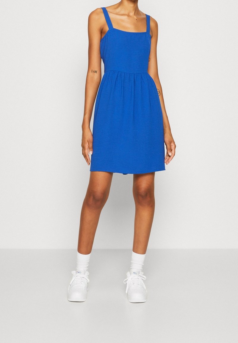 Vestido azul sin mangas con escote cuadrado, cuerpo ajustado y falda acampanada. Hecho de tela ligera, adornado con tirantes anchos.