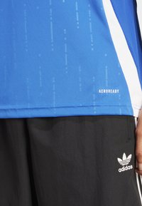 T-shirt de sport bleu avec des rayures verticales texturées, présentant un panneau latéral blanc et le logo "AEROREADY" à l'ourlet. Short noir avec le logo Adidas.