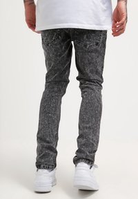 Faded black jeans with a slim fit, featuring a textured finish and back pockets, paired with white sneakers and a long white shirt.