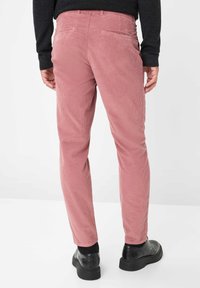 Pantaloni in velluto a coste rosa con taglio dritto, dotati di tasche posteriori e abbinati a scarpe nere, su uno sfondo neutro.