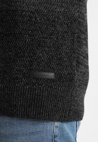 Jersey negro de punto con acabado texturizado, que presenta un dobladillo acanalado y un pequeño parche negro con el logo de Esprit en el lateral.