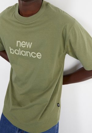 Olivengrünes Baumwoll-T-Shirt mit dem Text "new balance" in einem helleren Farbton. Kurze Ärmel und runder Halsausschnitt.