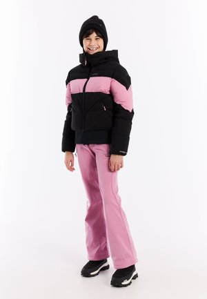 Schwarze und pinke isolierte Jacke mit Kapuze. Pinke Hose. Schwarze Stiefel mit grauen Akzenten. Lächelndes Kindermodell steht vor einem weißen Hintergrund.