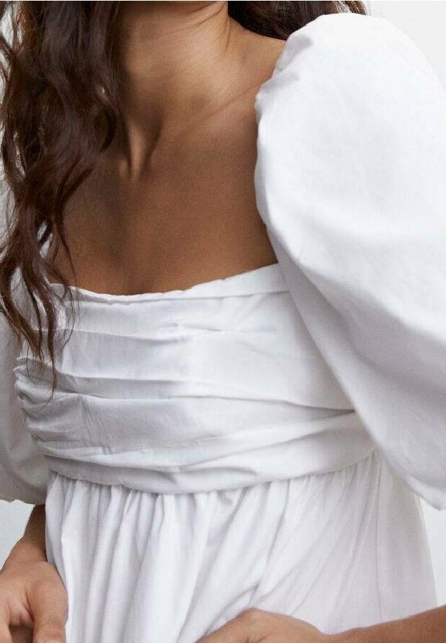 Weißes Kleid mit quadratischem Ausschnitt, Puffärmel und gerafftem Stoffdetail an der Brust, aus leichtem Material gefertigt.
