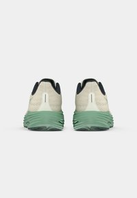 Deux chaussures de sport vues de l'arrière, présentant un dessus crème avec un design en tricot texturé, une semelle intermédiaire verte et des accents de talon foncé contrastants.