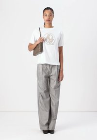 Weißes Kurzarm-T-Shirt mit Grafikdruck, kombiniert mit grauen karierter Weitbein-Hosen und einer kleinen beigen Handtasche. Schwarze Schuhe vervollständigen das Outfit.
