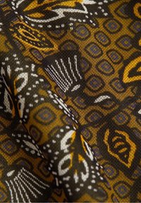 Textil med ett brunt och gult mönster som innehåller geometriska former och abstrakta designer, strukturerat stickat material med intrikata detaljer.