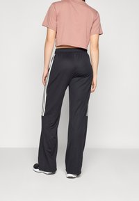 Svarta träningbyxor med vita sidostreifen, kombinerade med en kort, rosa t-shirt. Löst sittande, elastisk midja och mjukt, lätt material.