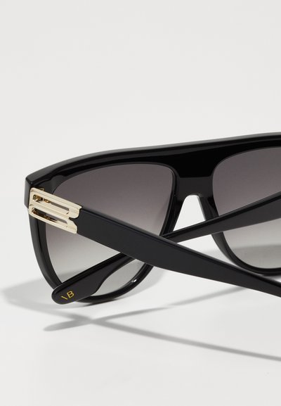 Óculos de sol pretos com lentes degradé, apresentando uma armação brilhante, design angulado e detalhes em dourado na dobradiça. Letras da marca em destaque no braço.