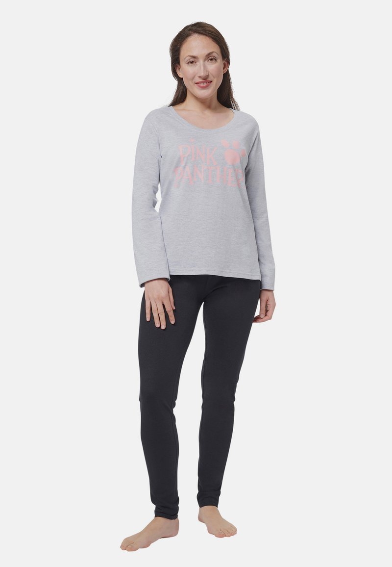 Donna in piedi a piedi nudi con una maglietta grigia a maniche lunghe del Pink Panther e leggings neri su uno sfondo bianco semplice.